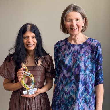 Two women stand together with one holding a colorful award